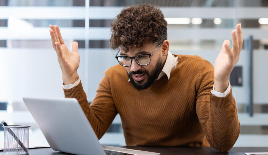 Why-I.T.-Problems-Never-Feel-Like-Just-IT. A man in an office sitting at a desk in front of a computer and frustrated with what he sees.